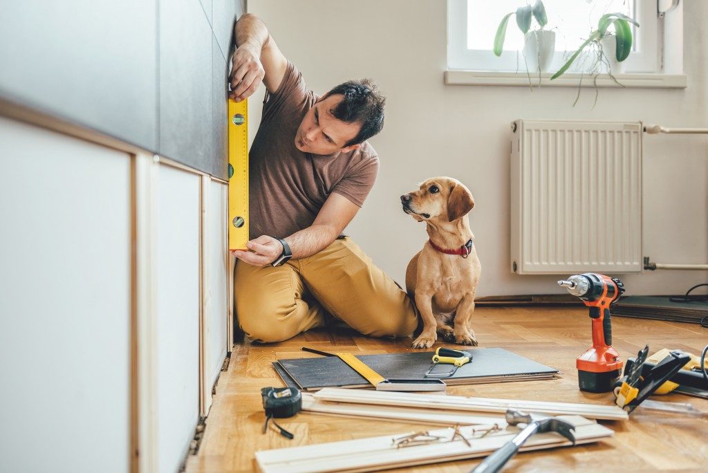 Man working on the wall of the house with a dog beside him