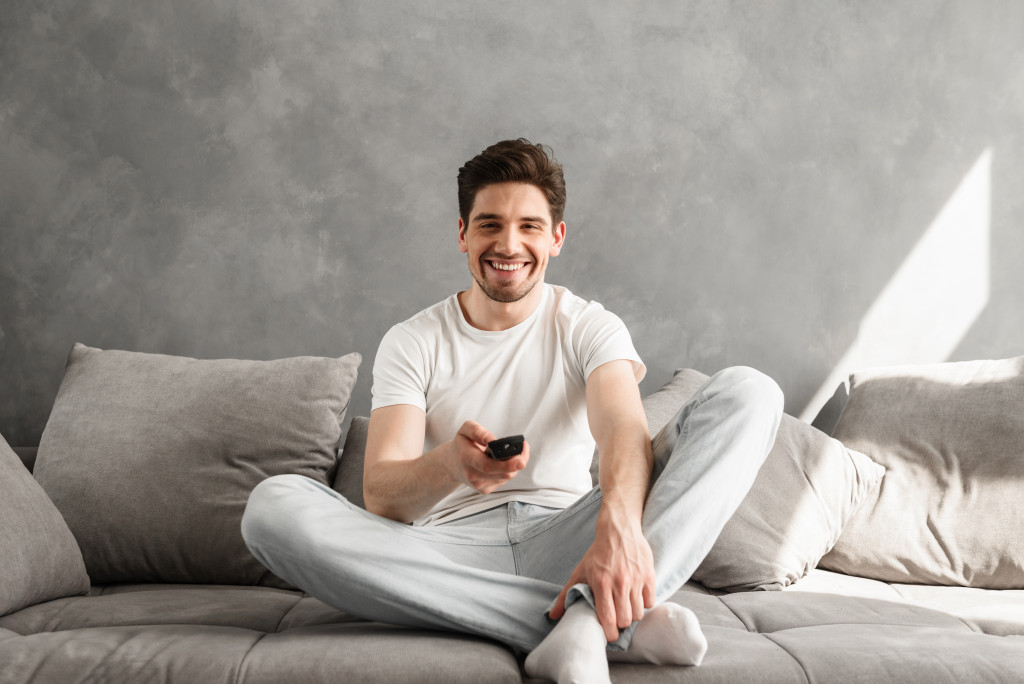 man holding a remote control for tv while sitting in a sofa