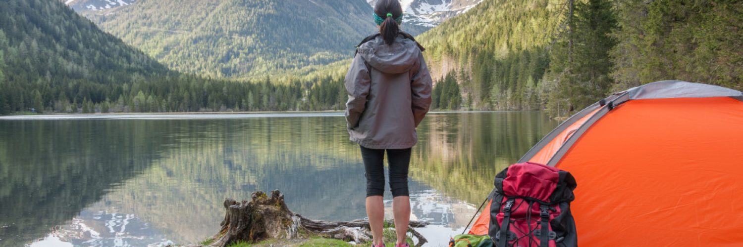 woman standing in front of a lake with a camping tent behind her