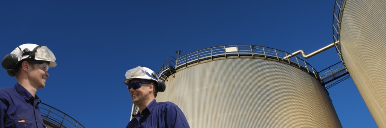 Oil and gas workers in front of large fuel storage tanks